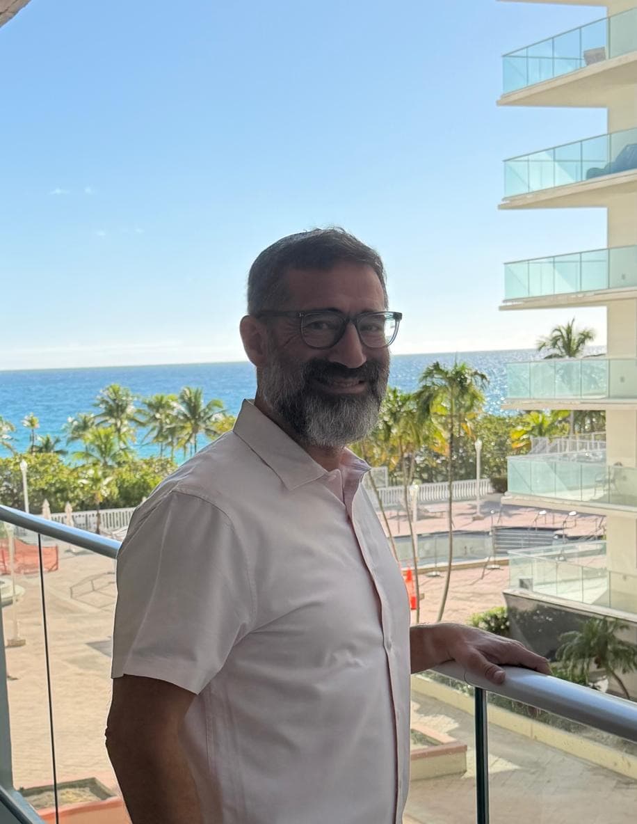 Chaim Backman, PT, resting a hand on a balcony rail, the ocean and palms behind him
