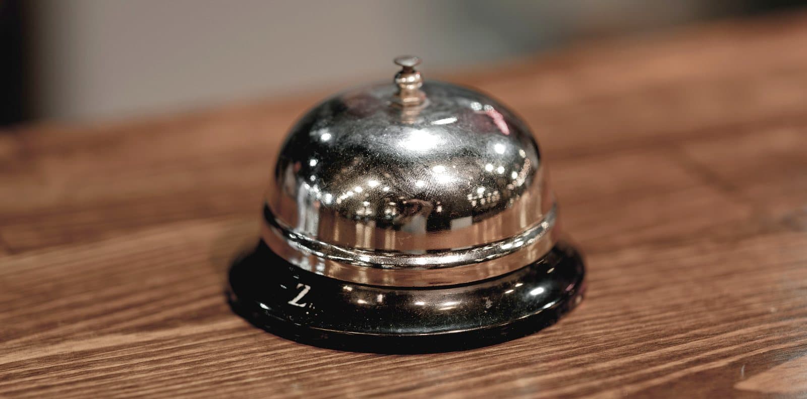 A polished reception bell on a wooden counter, lit warmly from one side