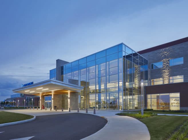 The glass-fronted entrance of a modern hospital building, lit at dusk