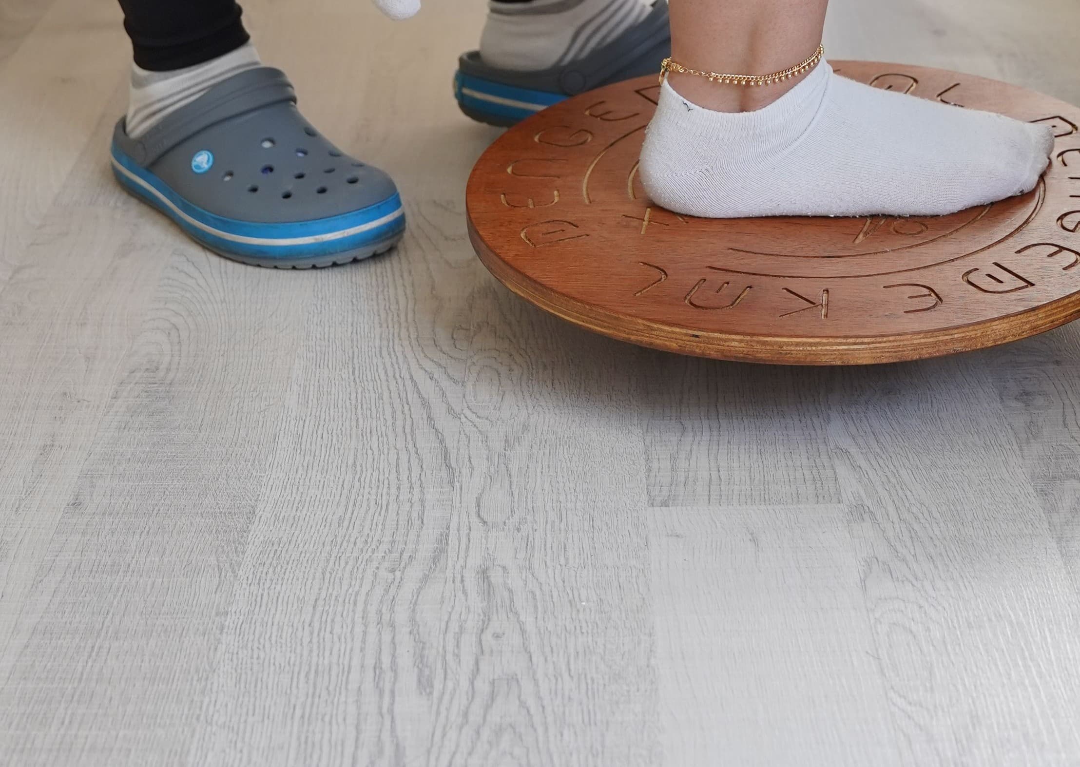 A close view of feet in white socks balancing on a round wooden balance board, testing stability