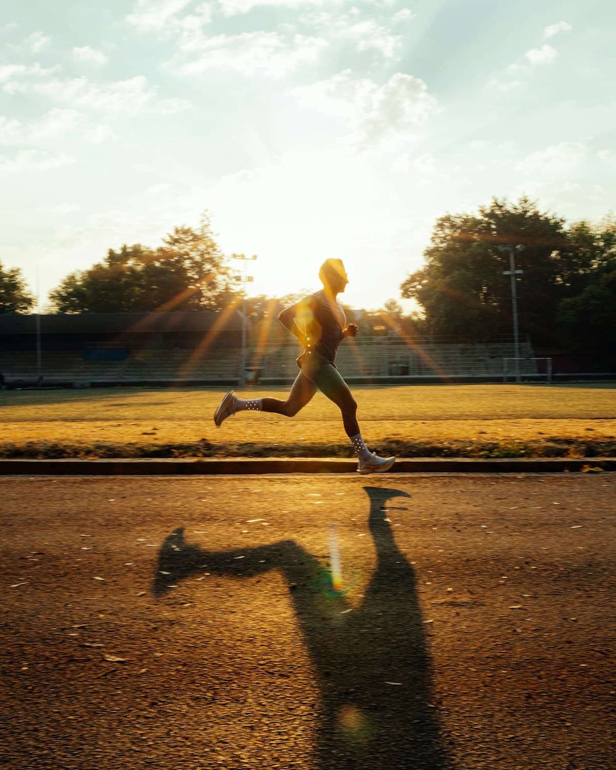 A runner in silhouette, mid-stride on a track at golden hour